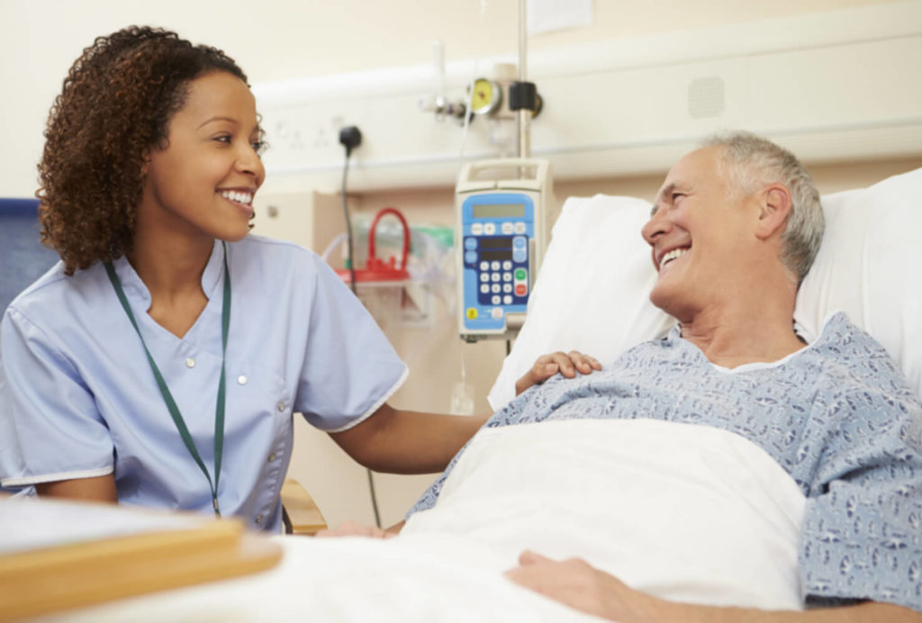 A friendly smiling nurse talking to a patient who is in a hospital bed.