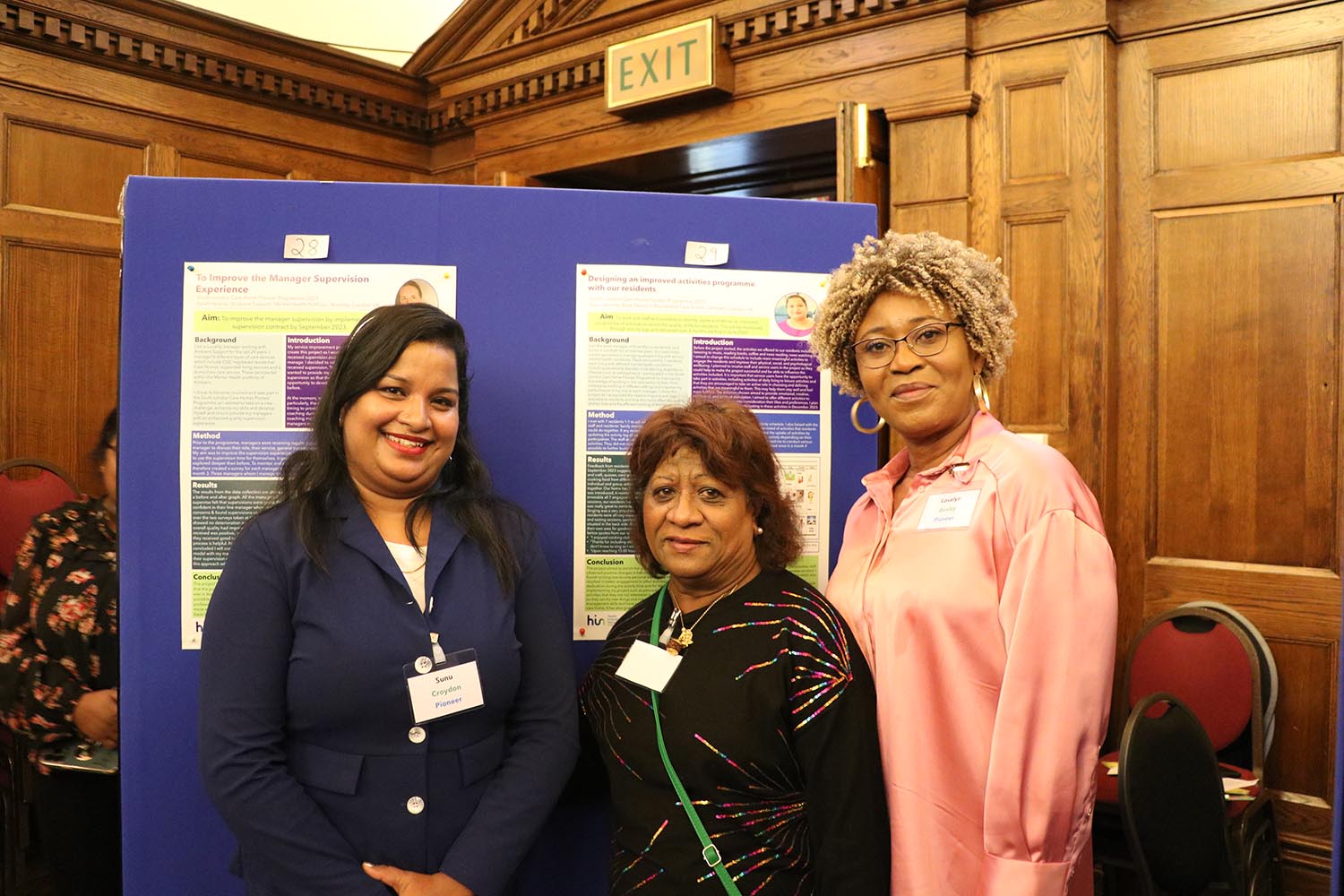 Three Pioneers standing in front of their posters at the December 2023 celebration event