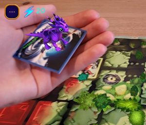 An open hand holding a 3D dragon and hovering above a board game