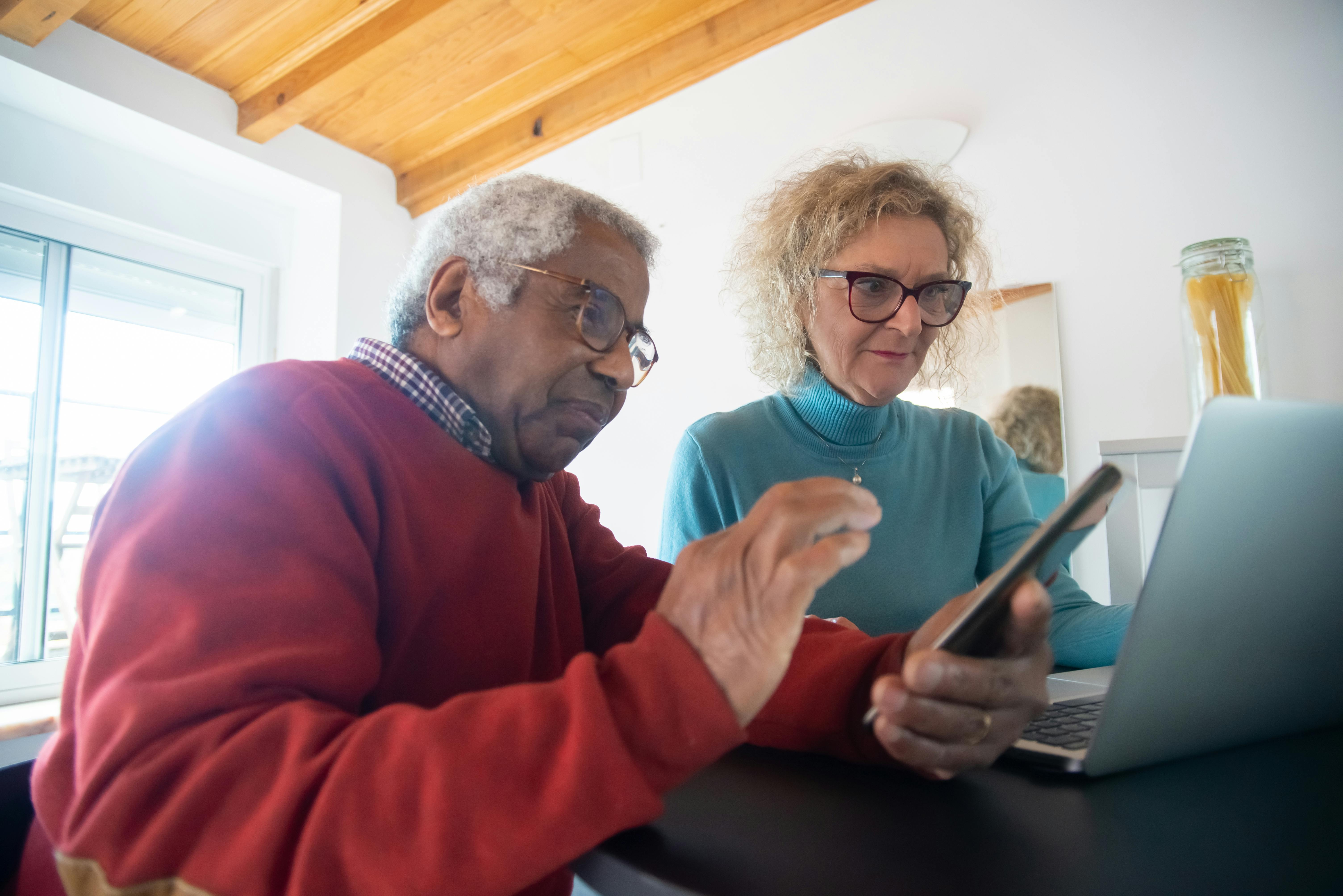 Two elders utilising a laptop and a mobile device.