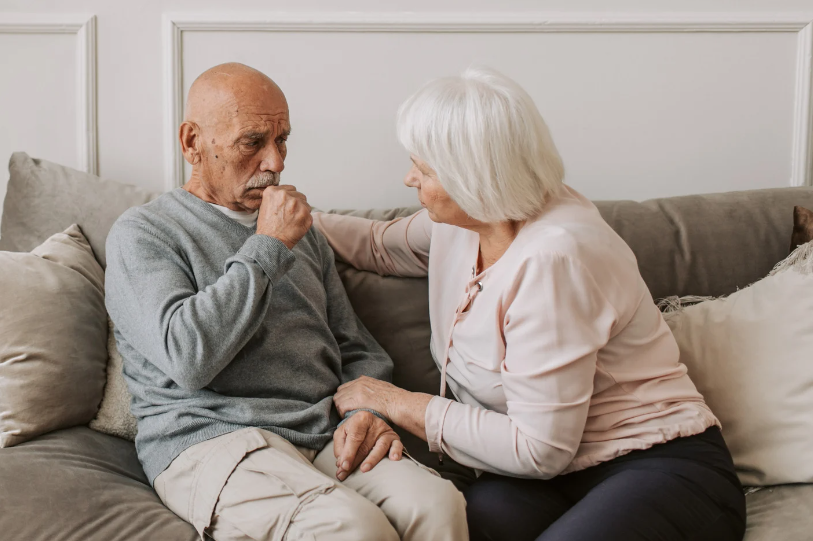 Image of a man coughing, and a woman holding his arm.